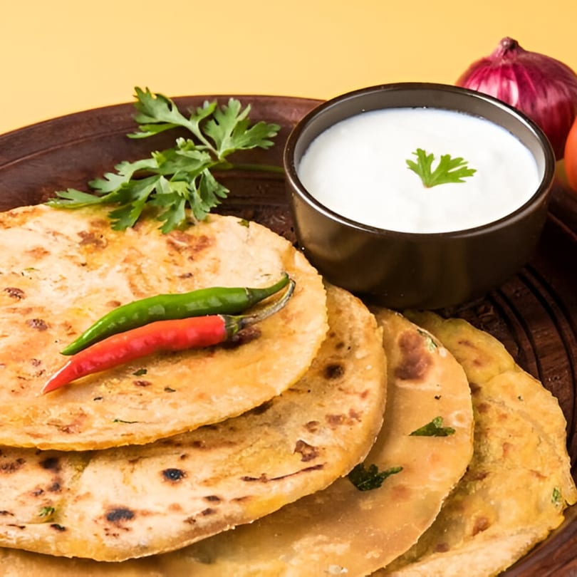 Masala Express parathas with green and red chilies, cilantro, and yogurt dip on a wooden plate.