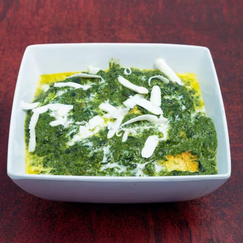 Masala Express's Palak Paneer, a vibrant green spinach curry with white paneer cheese, in a white bowl.