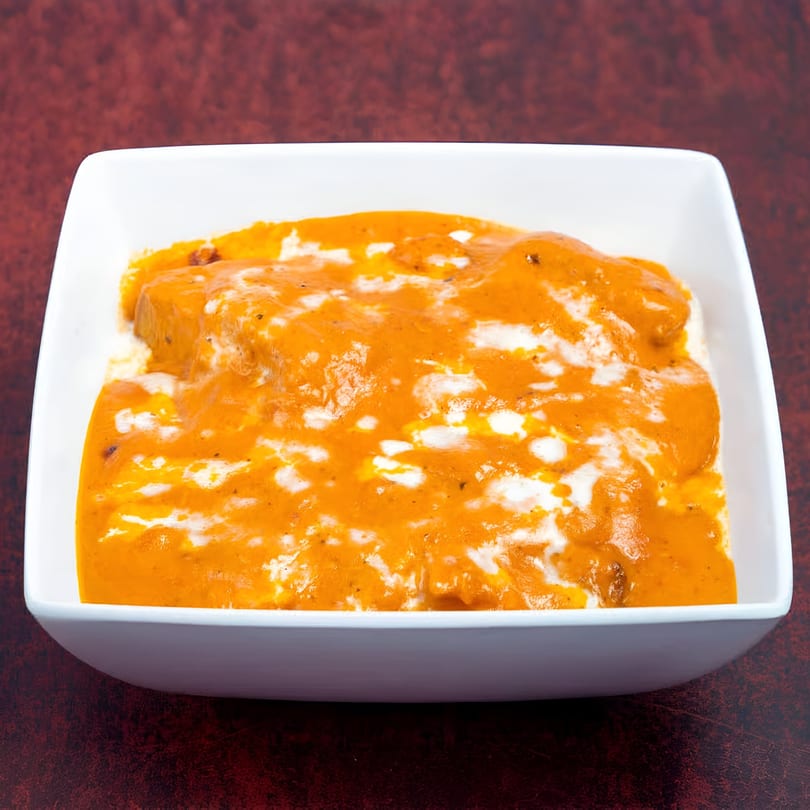 Masala Express's creamy orange Indian curry with white swirls, served in a white square bowl.